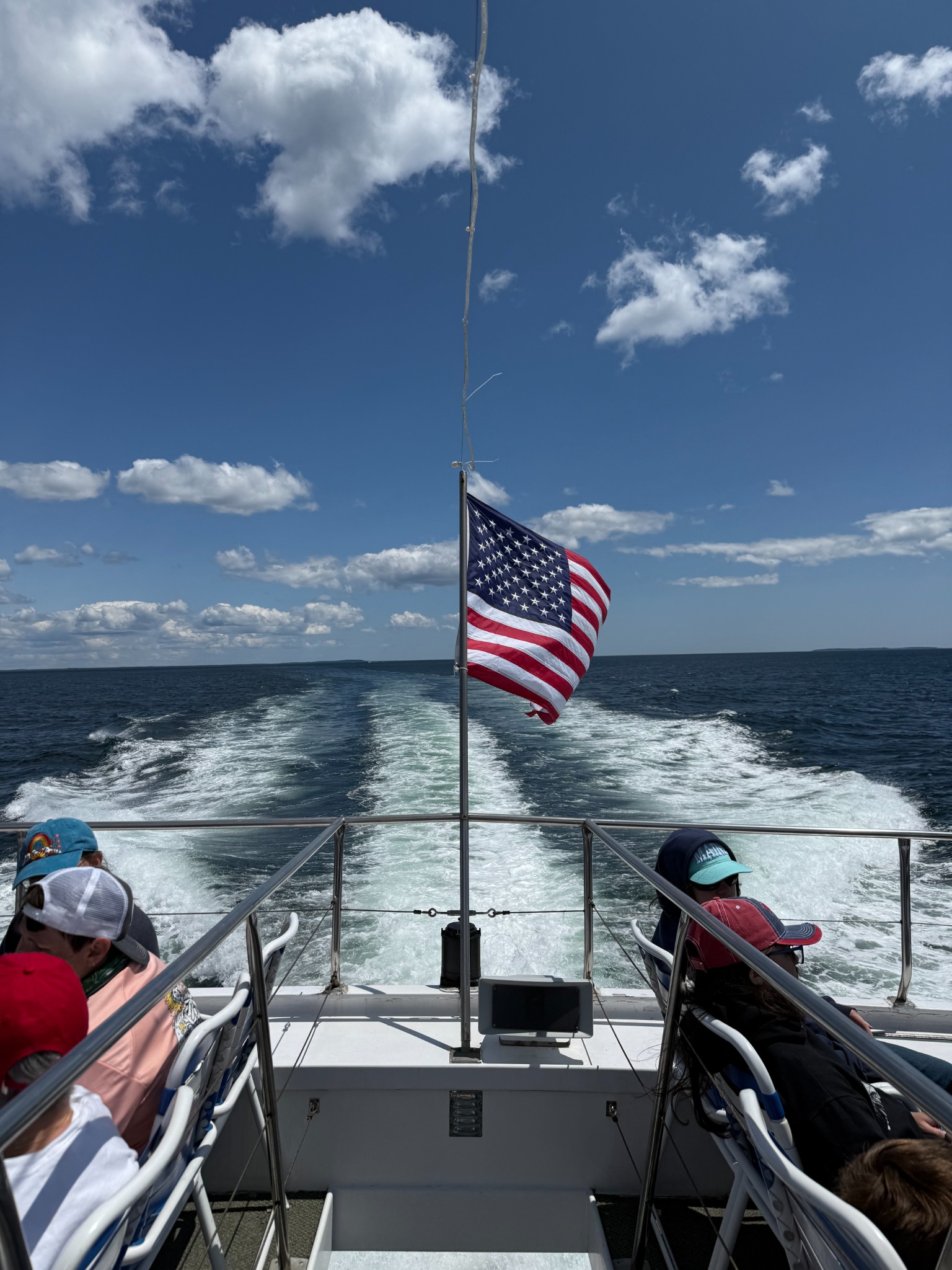 View from a passenger boat, with an American flag above the wake and open water beyond